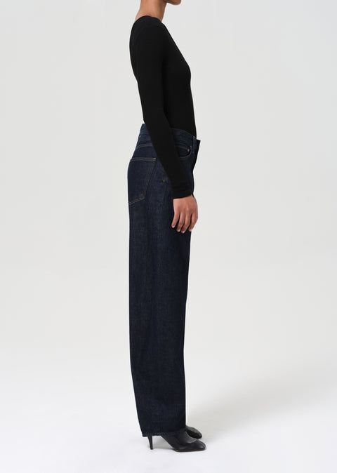 Person wearing a black long-sleeve top and dark blue, wide-leg jeans on a white background side view 
