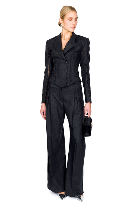 Woman posing to the side wearing gray double breasted, long-sleeve top paired with matching trousers that are pleated down the middle