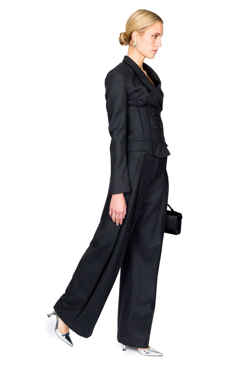Side view of gray double breasted, long-sleeve top paired with matching trousers that are pleated down the middle
