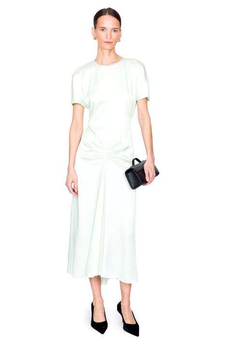 Woman posing in a light green satin midi dress holding a black handbag on a white background