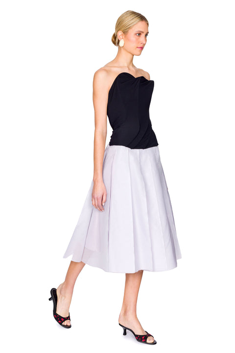 Side view of woman stepping in black strapless top and midi skirt.