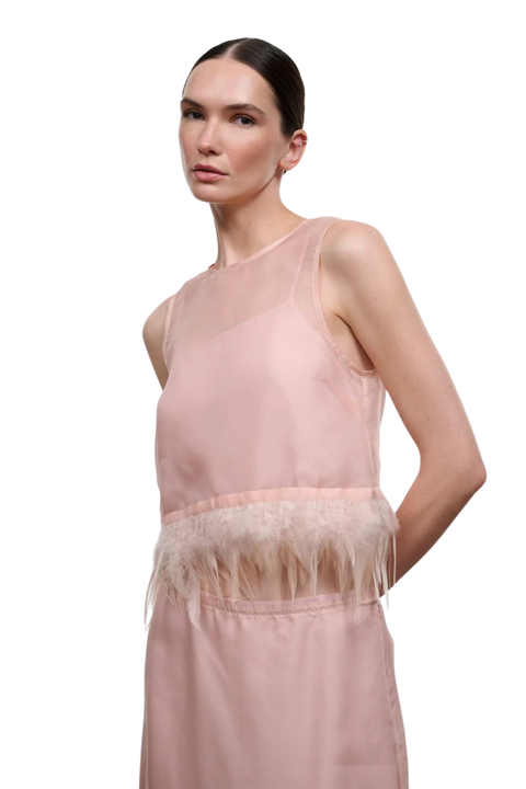 A model wearing a sleeveless dusty pink top with a sheer mesh neckline and a feathered waistband, photographed against a solid white background.