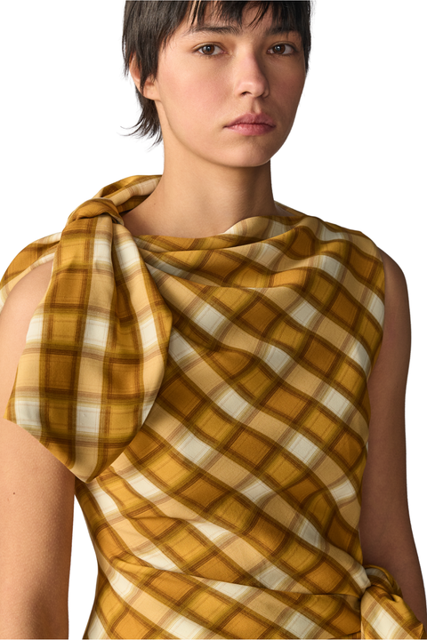 A model wearing a draped, sleeveless top with a mustard yellow and cream plaid pattern, shown against a plain white background.