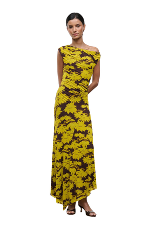 A woman modeling a one-shoulder maxi dress with a bold yellow and dark brown abstract floral pattern, photographed against a solid white background.
