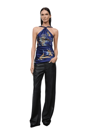 A model wearing a halter-neck top with a blue and gold print, paired with black wide-leg pants, set against a plain white background.