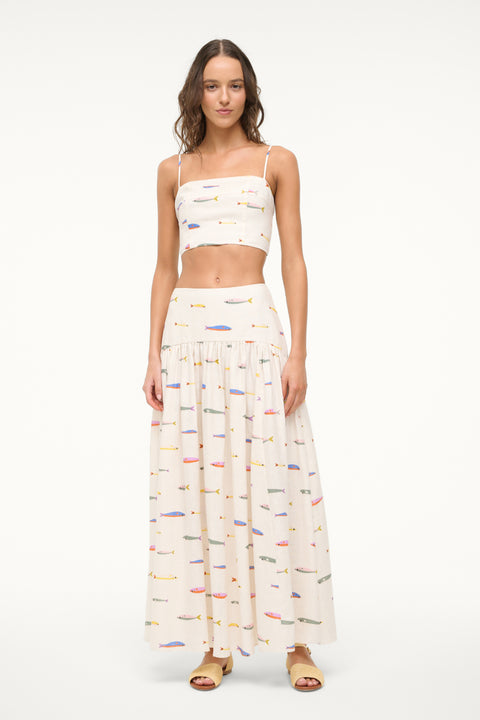 Woman wearing a cream spaghetti strap crop top that features a colorful fish design, paired with a matching maxi skirt. 