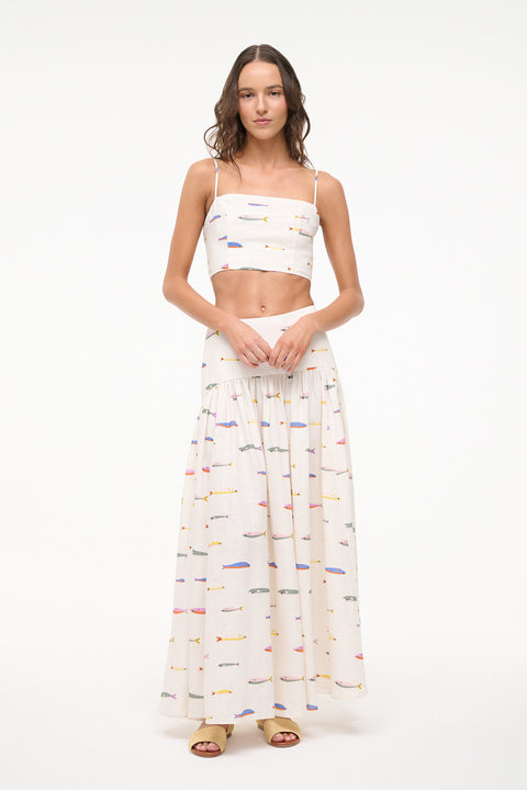 Woman wearing a cream spaghetti strap crop top that features a colorful fish design, paired with a matching maxi skirt. 