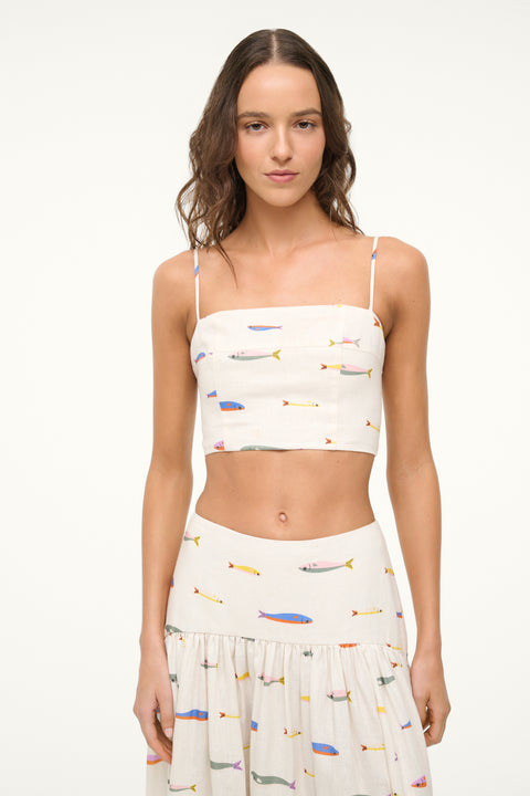Close up of a woman wearing a cream spaghetti strap crop top that features a colorful fish design, paired with a matching maxi skirt. 