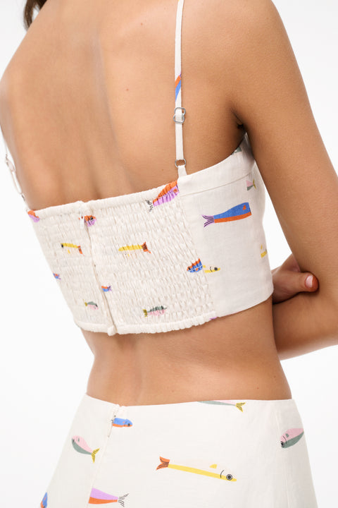 Detail shot of the back view of a woman wearing a cream spaghetti strap crop top that features a colorful fish design, paired with a matching maxi skirt. 