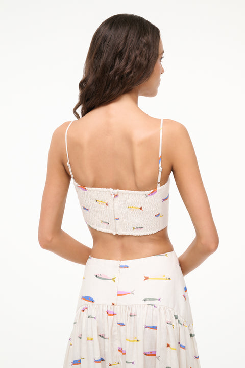 Close up back view of a woman wearing a cream spaghetti strap crop top that features a colorful fish design, paired with a matching maxi skirt. 