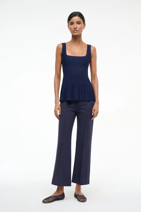 Woman wearing a navy knit tank to that features a square neck and sheer, pleated bodice, paired with cropped navy pants. 