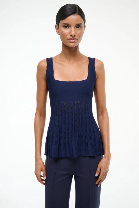 Close up of a woman wearing a navy knit tank top that has a textured hem, square neck with a sheer pleated bodice, paired with navy pants. 