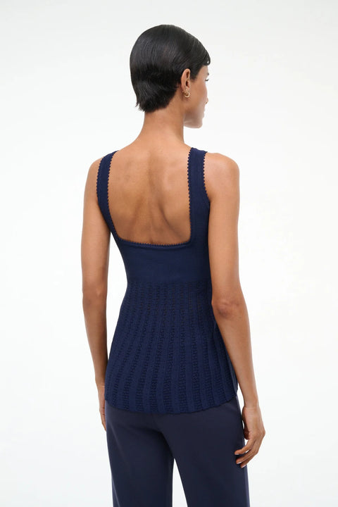 Back view of a woman wearing a navy knit tank top that features a low square back and pleated bodice, paired with navy pants. 
