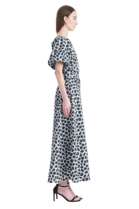Woman facing the right wearing a blue polka dot maxi dress with short sleeves a white background
