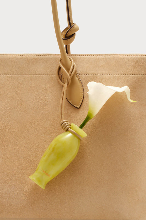 Small decorative calla lily bag charm on a bag against a beige background