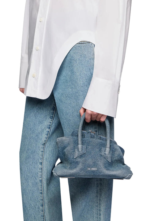 Person wearing a white shirt and blue jeans holding a matching mini denim handbag 