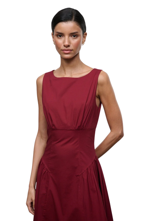 A woman modeling a sleeveless, scoop-neck midi dress in a deep burgundy red, shown against a plain white background.