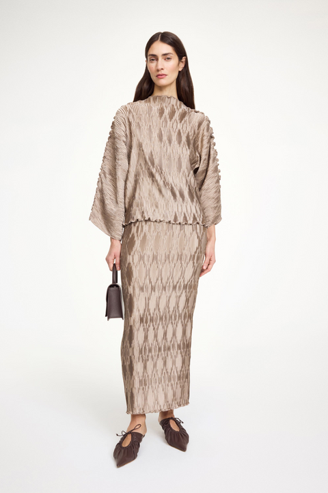 Woman wearing a textured beige top that features wide sleeves and a boatneck neckline, paired with a matching skirt.