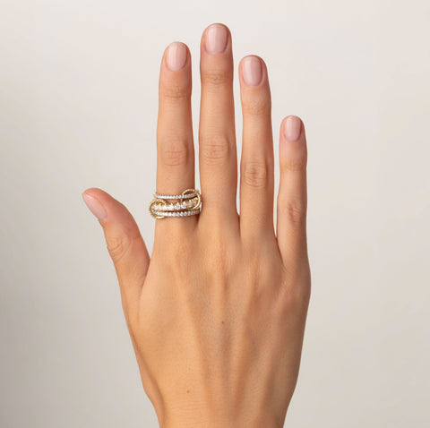 A woman's hand wearing a Spinelli Kilcollin Junia ring that features a 1.7mm white gold band pave with diamonds, a 2.6mm yellow gold band pave with diamonds, and a 2.3mm white gold bands pave with diamonds, connected by two yellow gold connectors pave with diamonds. 