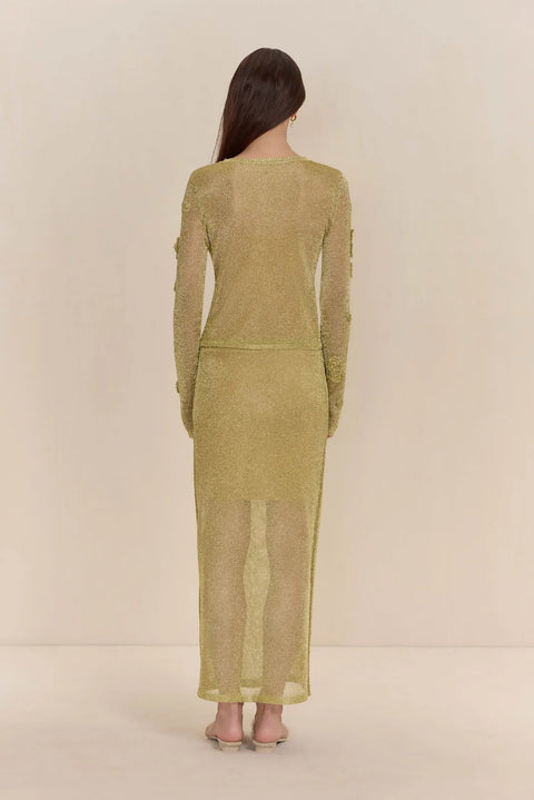 Back view of a woman wearing a sheer, gold knit cardigan paired with a matching midi skirt.