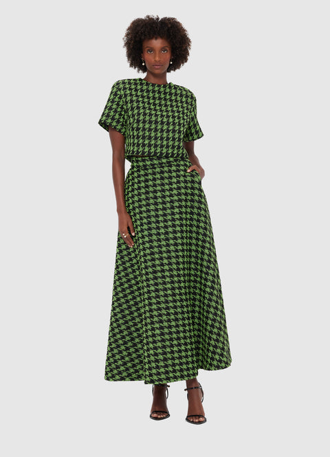Woman standing in contrapposto wearing a green and black houndstooth tweed short sleeve crop top and matching A-line maxi skirt, paired with black heels. 
