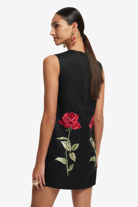Woman showing the back of the black sleeveless dress with red rose embroidery on a white background