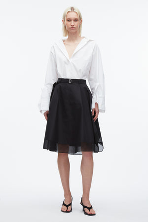 Woman wears black midi skirt with belt featuring organza overlay and white cotton top.