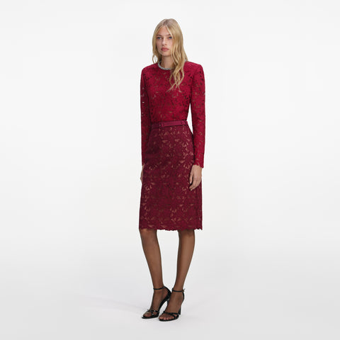 Woman posing wearing a red lace long sleeve top and matching red lace midi skirt on a white background