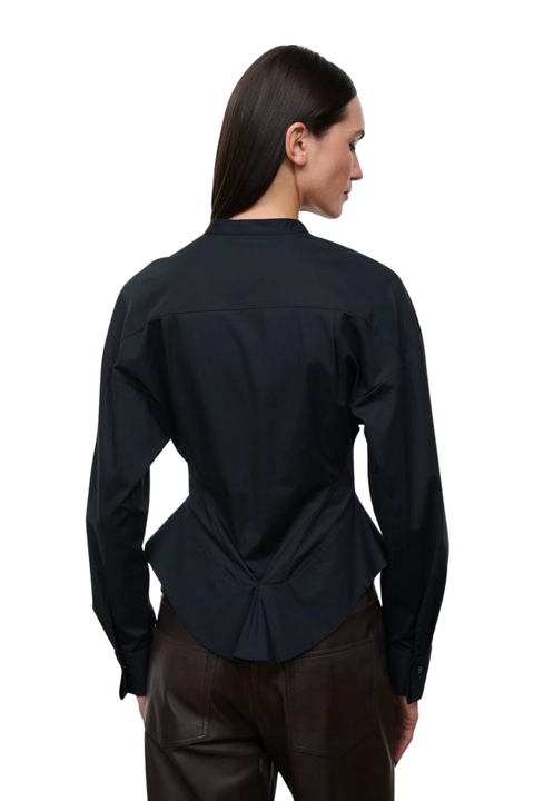 A woman shown from the back wearing a black long-sleeve button-up shirt with a gathered peplum-style back detail, paired with dark brown pants, against a plain white background.