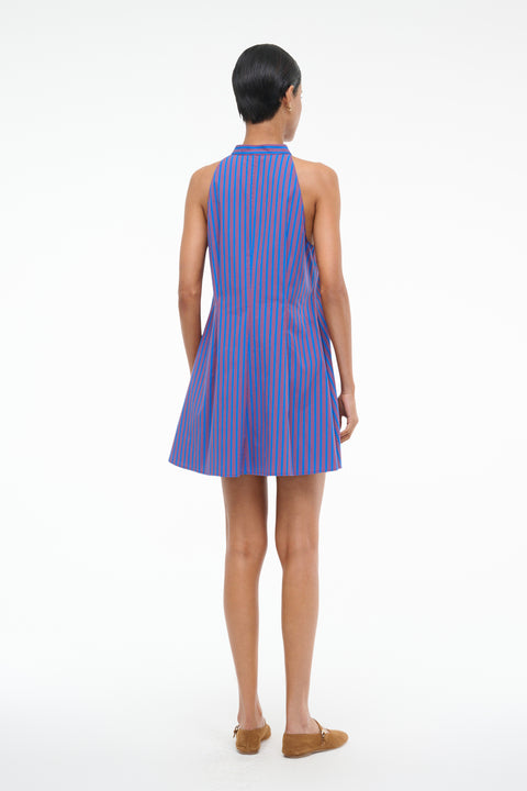 Back-facing woman wearing a red and blue stripe poplin mini dress that features a stand collar and front button closure, paired with brown flats. 