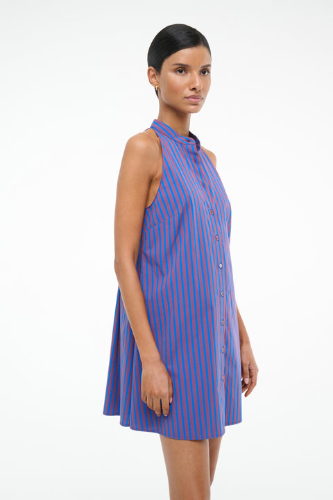 Side-facing woman wearing a red and blue stripe poplin mini dress that features a stand collar and front button closure, paired with brown flats. 