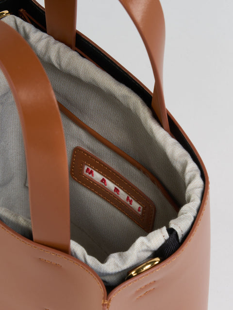 Close-up of a brown handbag with visible brand name on a light gray background