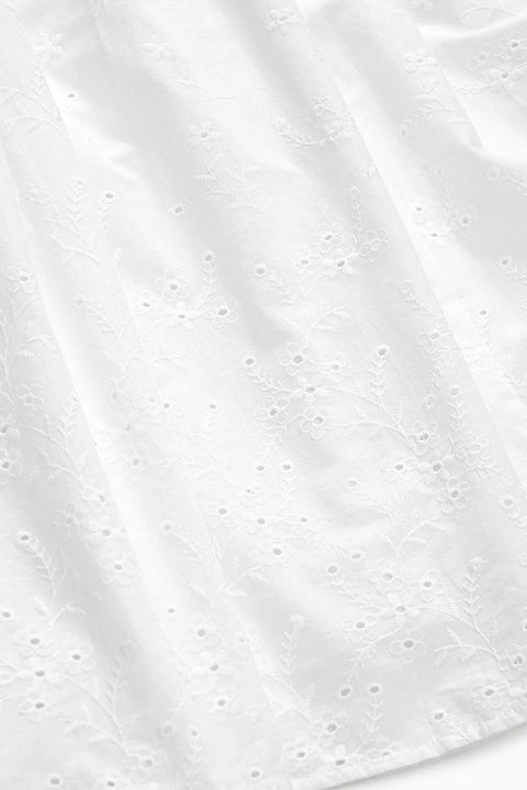Detail shot of the white eyelet fabric of a maxi skirt with a curved yoke waist. 