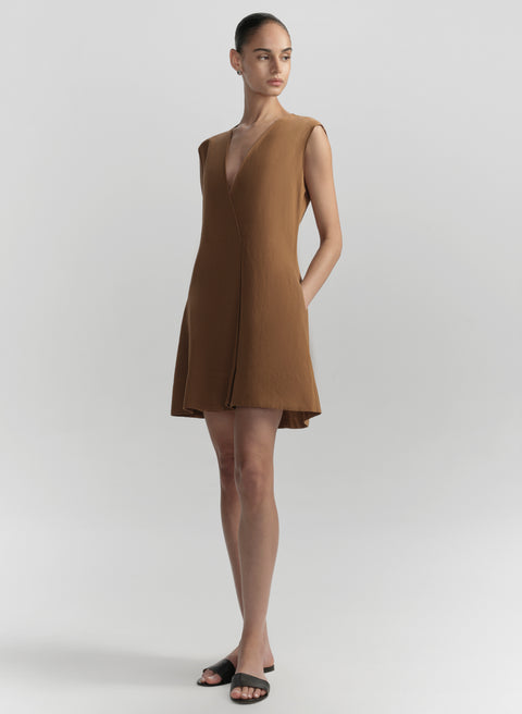 Woman wearing a high neck white sleeveless dress from the side on a plain background