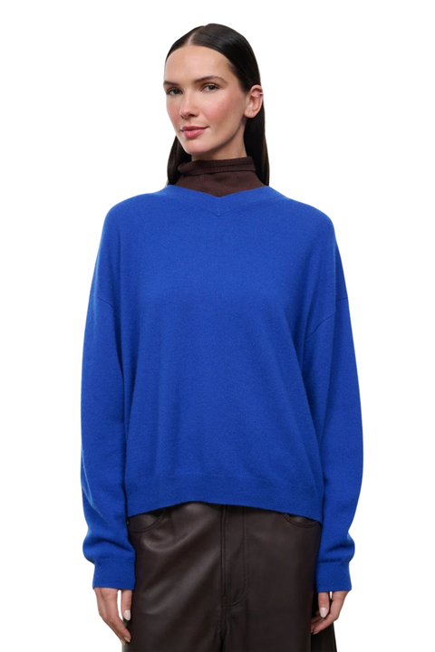 A woman modeling a vibrant royal blue knit sweater layered over a dark brown mock neck, paired with dark brown pants, against a plain white background.