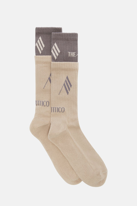 Flat lay of a pair of cream and taupe socks that have a layered effect design and contrasting color logos. 
