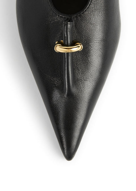 Close-up of a black pointed-toe leather shoe with a small gold metal accent at the vamp, shown on a white background.