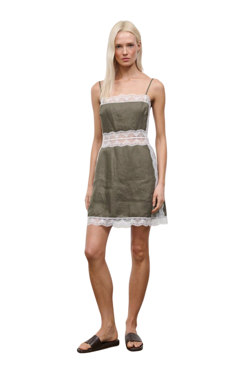 A woman wearing a taupe-green mini dress with white lace detailing on the waistline and neckline