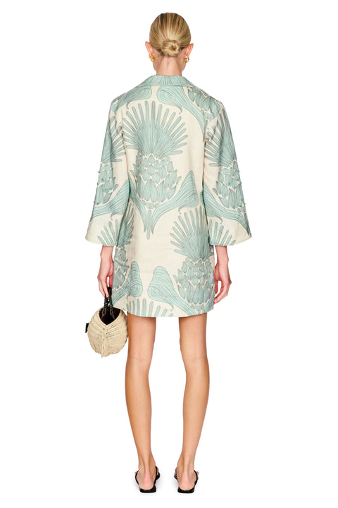 Woman wearing a light green and white patterned tunic dress on a white background back angle
