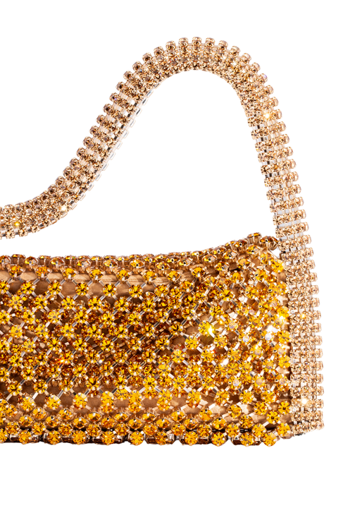A close-up of a rhinestoned evening bag with a curved top handle, covered in shimmering gold and amber rhinestones on a white background.