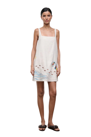 A woman wearing a mini dress with embroidered beach details 