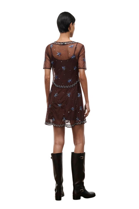 Woman wearing a brown sheer mini dress with embellishments on a white background back angle