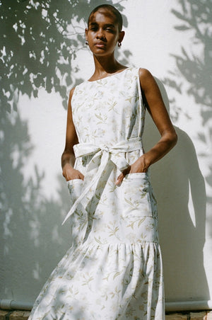 Model with hands in front pockets of the white printed midi shift dress with belt.