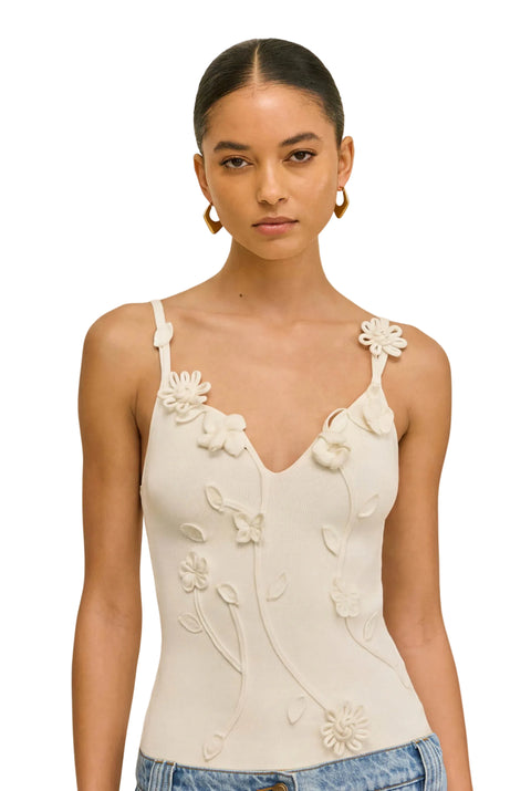 Woman wearing a cream-colored tank top with floral embellishments on a beige background