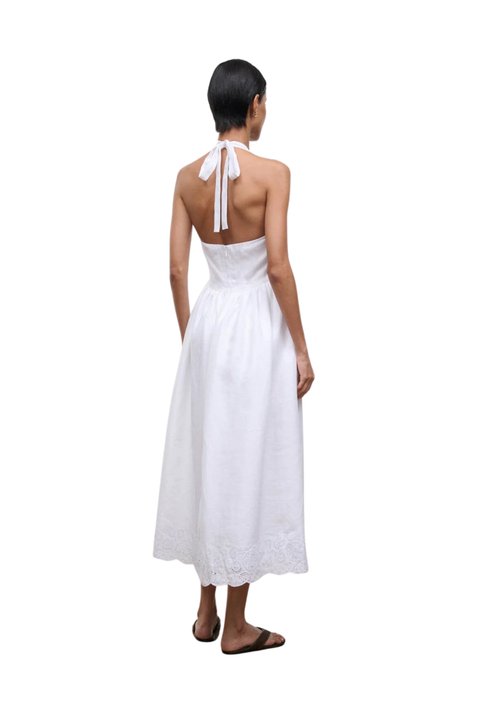 Woman wearing a long white halter neck dress on a white background back angle