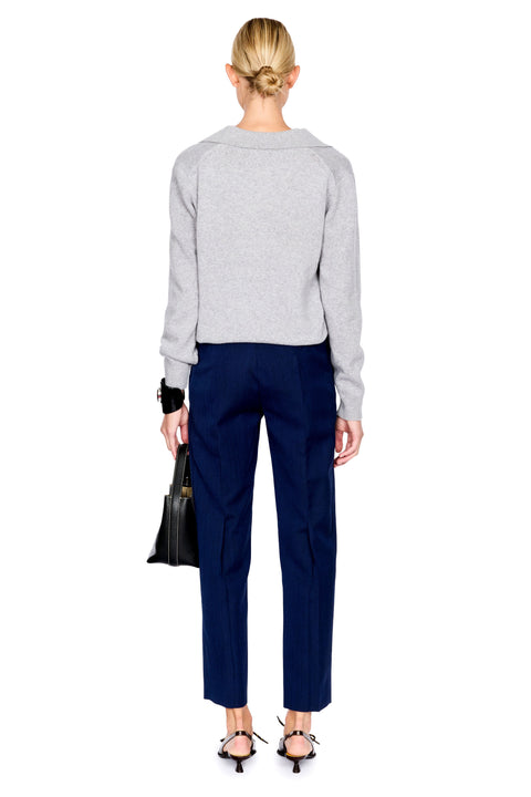 A woman shown from the back wearing a light gray cropped knit sweater and navy blue cropped trousers, holding a black handbag against a plain white background.