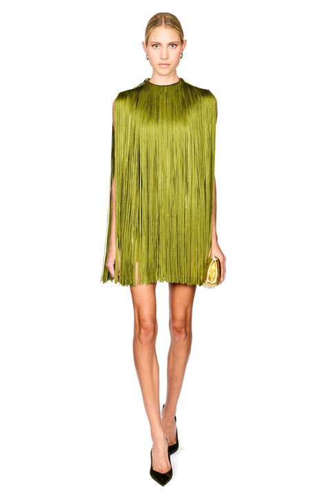 A model stands against a white background wearing a sleeveless olive green mini dress with a high mock neck, paired with dark green pointed-toe heels and holding a small gold clutch.