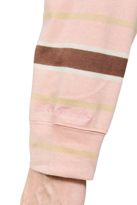 Close up of a "Tanner Fletcher" logo embroidered on the sleeve of a long sleeve pink and brown stripe t-shirt