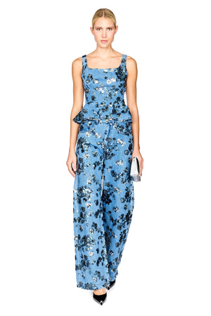 A model wearing a sleeveless denim floral top with a peplum waist with matching jeans, photographed against a solid white background.