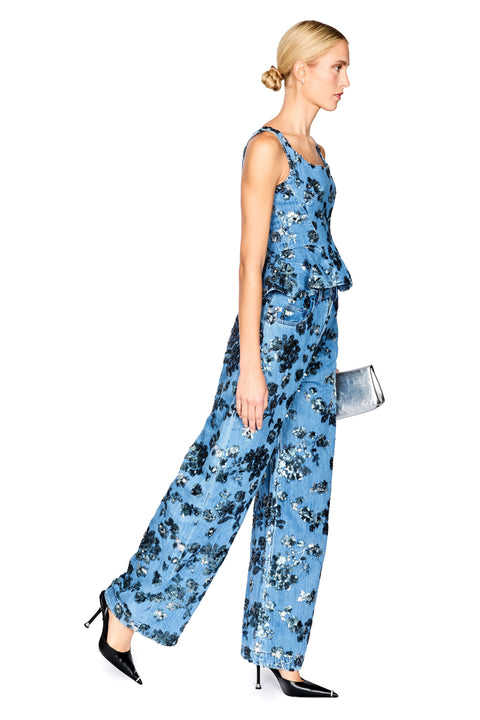 A model wearing a sleeveless denim floral top with a peplum waist with matching jeans, photographed against a solid white background.
